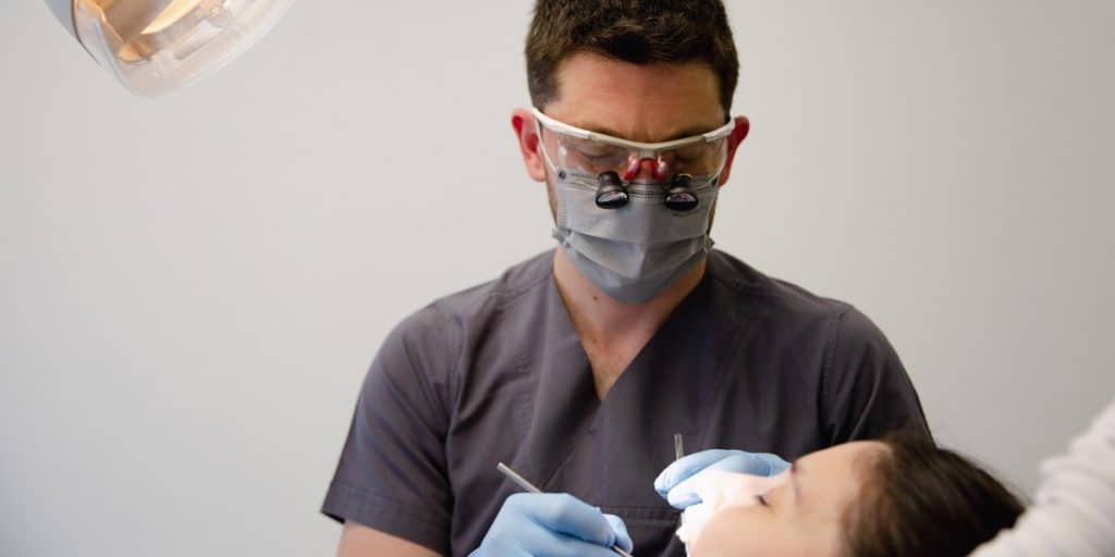 Dentist in dental magnifying glasses and mask while doing treatment.