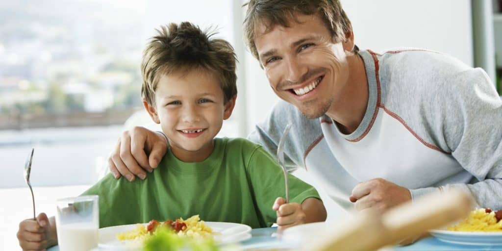 Father and son eating healthy food and smiling at camera.