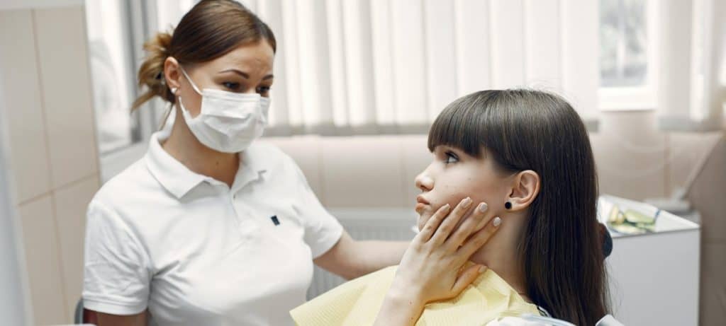 Patient holding cheek in pain looking at dental hygienist.
