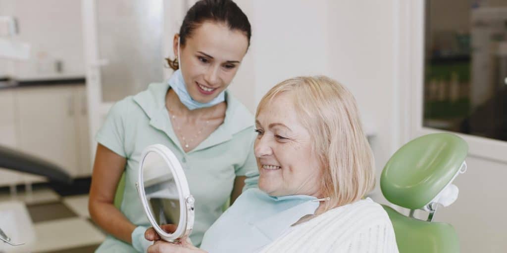 Dental hygienist looking at senior patient smiling in the mirror.