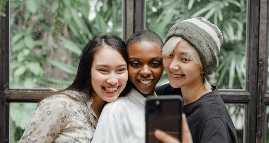Three women with beautiful smiles taking a selfie with a smartphone.