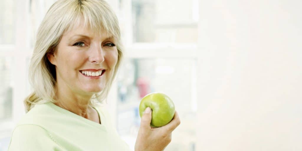 Mature woman smiling while holding a green apple.