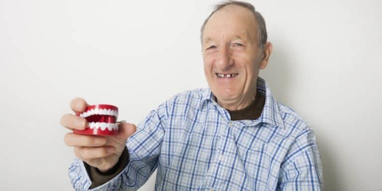 Senior man smiling while holding a plastic teeth model.