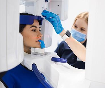Hygienist assisting female patient into modern dental X-ray machine.