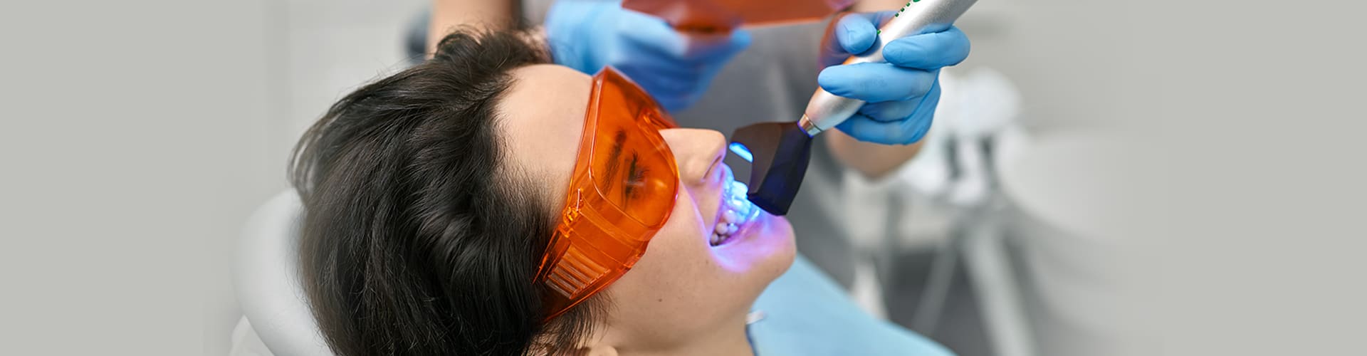Teeth whitening blue light procedure on a smiling female patient.