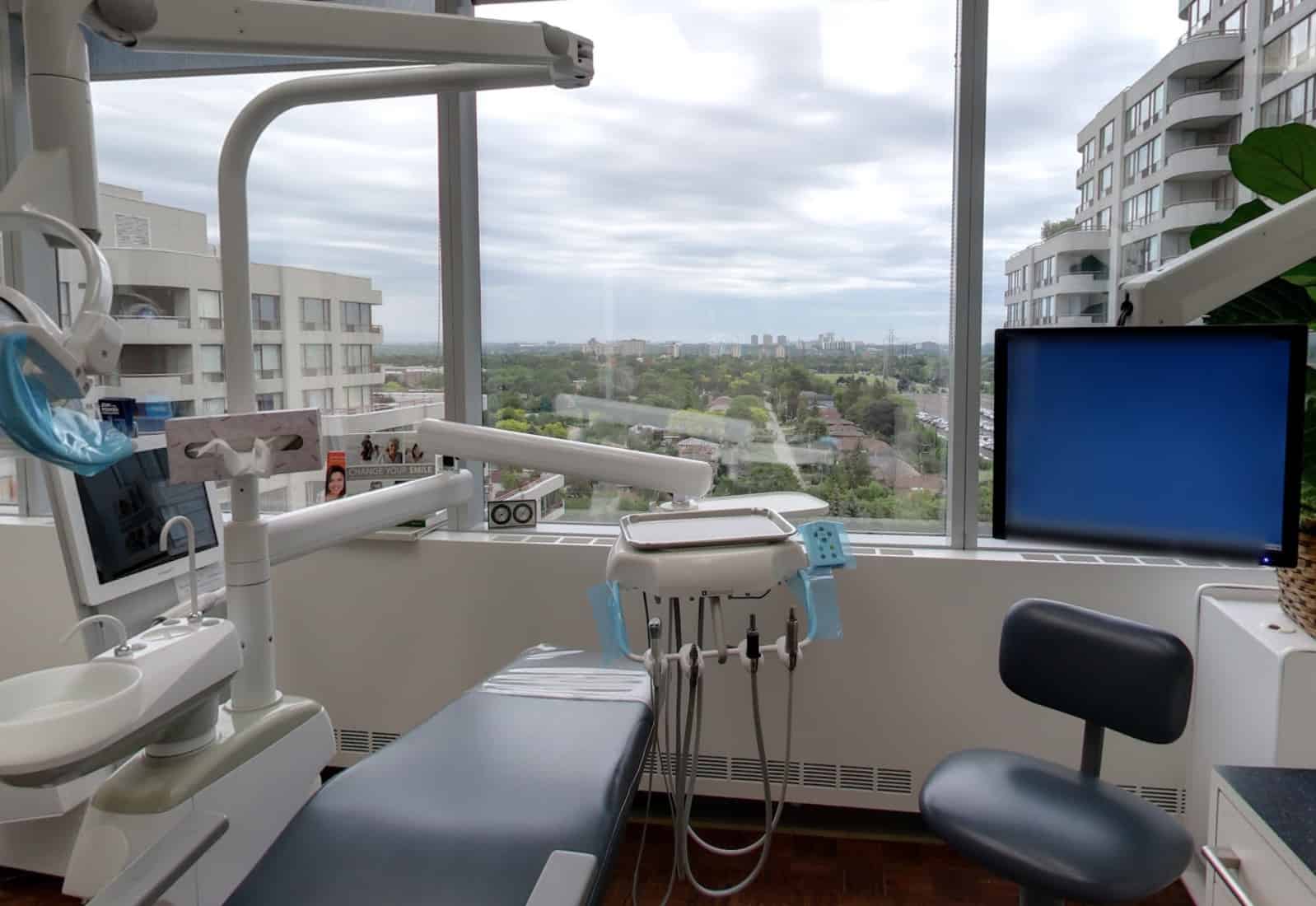 Dentist's chair and digital screen inside clinic overlooking outdoor scenery.