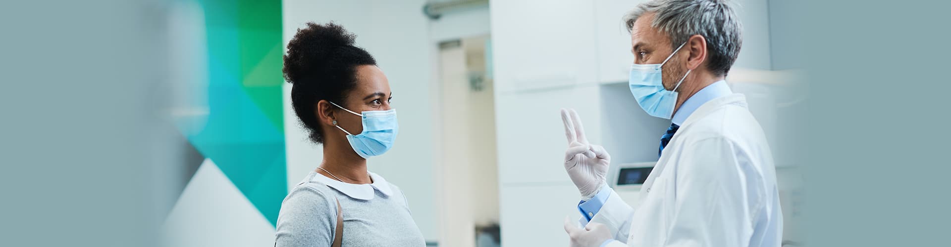 Masked dentist and patient talking while facing each other after Covid-19 protocol.