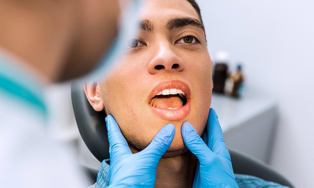 Dental professional guiding male patient's chin down to open mouth.