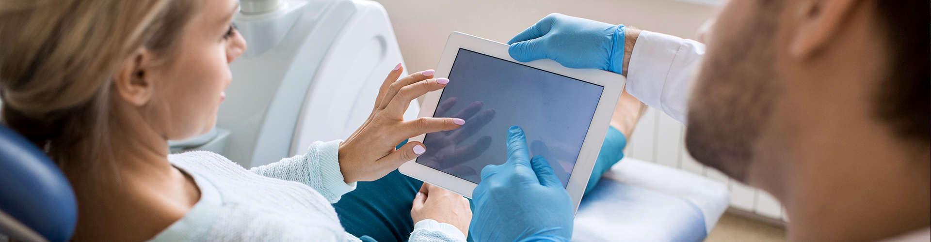 Dental professional and female patient pointing at digital tablet.