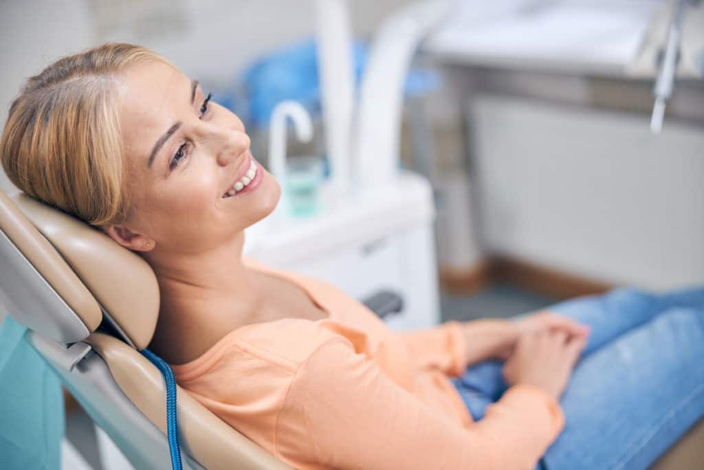 Smiling female patient waiting in the dentist's chair for a dental procedure.