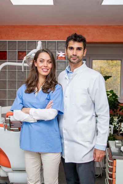Male and female dental professionals standing inside a dental office.